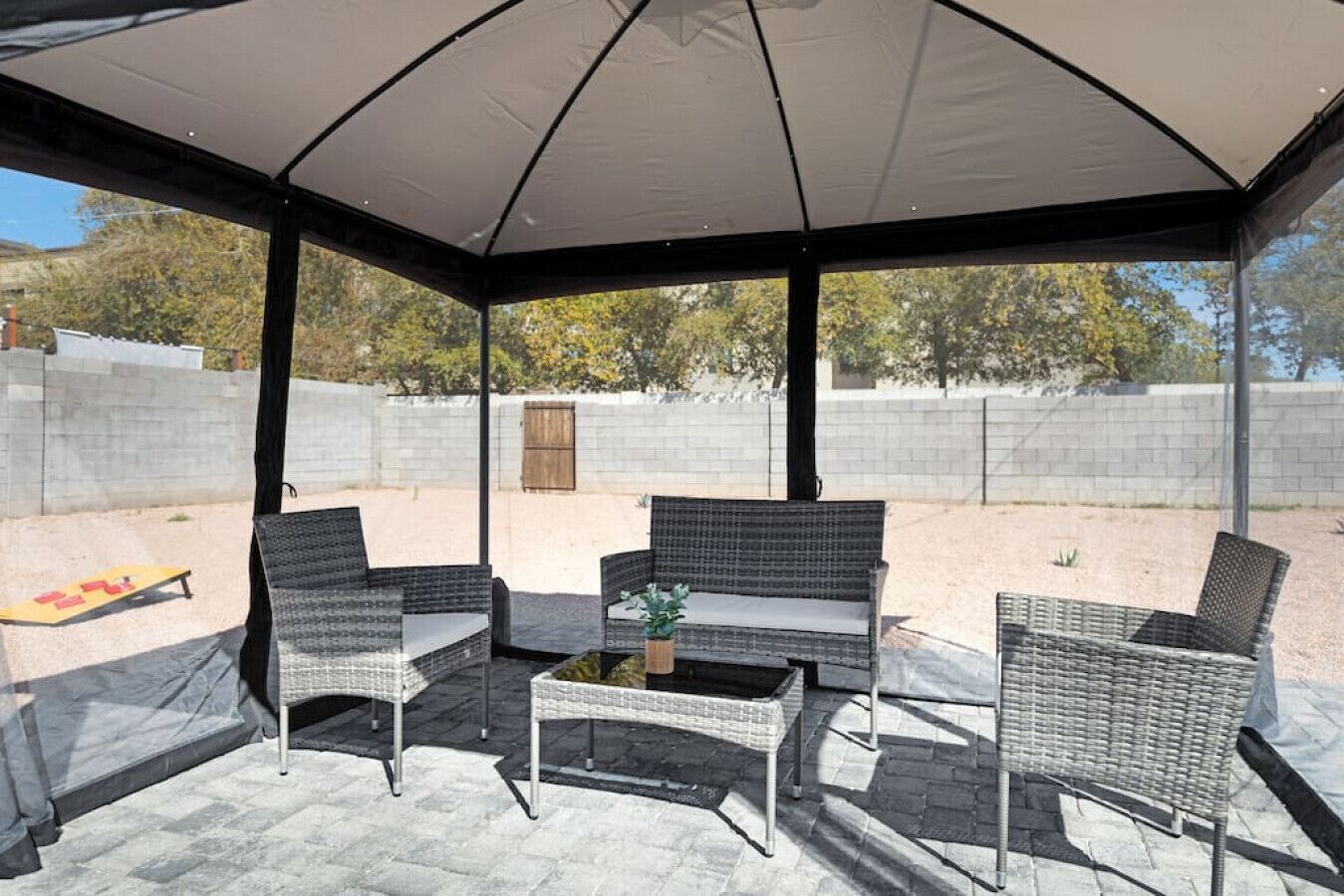 An outdoor patio with a covered seating area, including wicker chairs and a table with a vase.