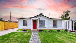 Une maison de plain-pied avec une porte rouge, un revêtement extérieur blanc et un porche à l’avant.