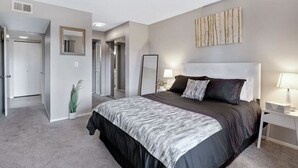 Un dormitorio con una cama grande, una mesita de noche, un espejo y una puerta que da a otra habitación.