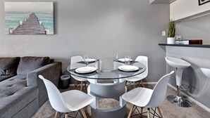 Un comedor moderno con una mesa de vidrio, sillas blancas y vistas al océano a través de una ventana.