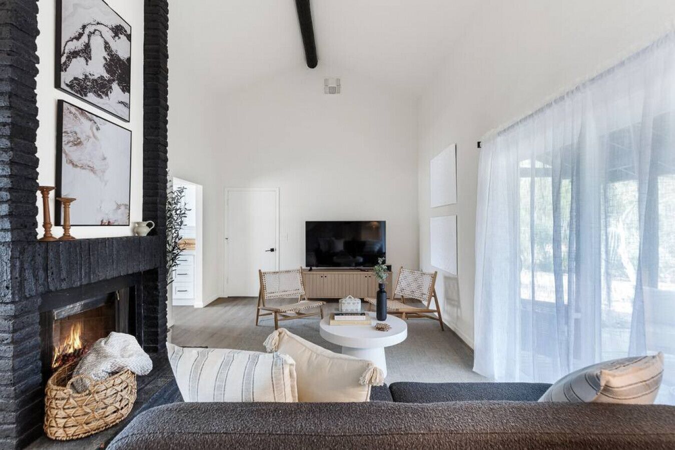 A modern living room with a fireplace, a television, and a large window with sheer curtains.