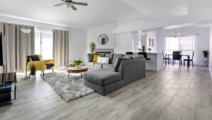 En moderne stue med en grå sofa, en gul lænestol og et spiseområde med bord og stole.