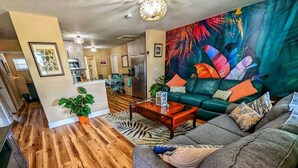 A living room with a sofa, coffee table, and a vibrant tropical mural.
