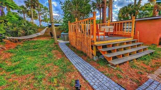 A wooden deck with steps leading to a covered seating area, surrounded by a garden with a paved path.