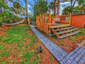 A wooden deck with steps leading to a covered seating area, surrounded by a garden with a paved path. - Tropical Lagoon Getaway: River View ~ Hot Tub (Titusville)