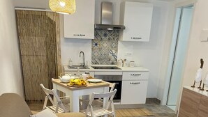A modern living room with a brown sofa, white cushions, a small round table, and a kitchen area with white cabinets and a tiled backsplash. - Piccola casetta, appena ristrutturata, un vero gioiellino, tra le vie del borgo. (Castellammare del Golfo)