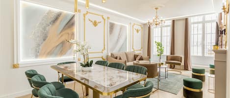 A spacious dining area with a marble table, green upholstered chairs, and gold accents.