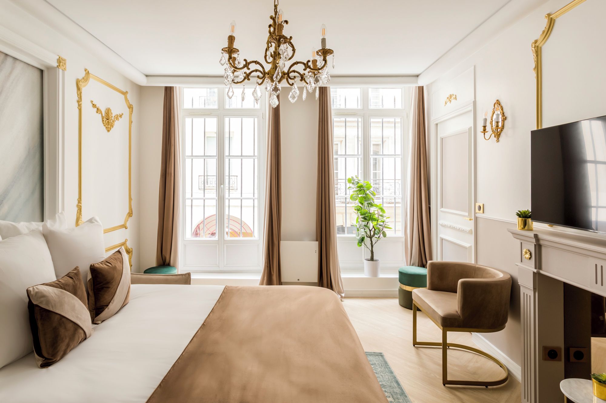 A spacious bedroom with a large bed, a sitting area, a television, and a view of the city through large windows.