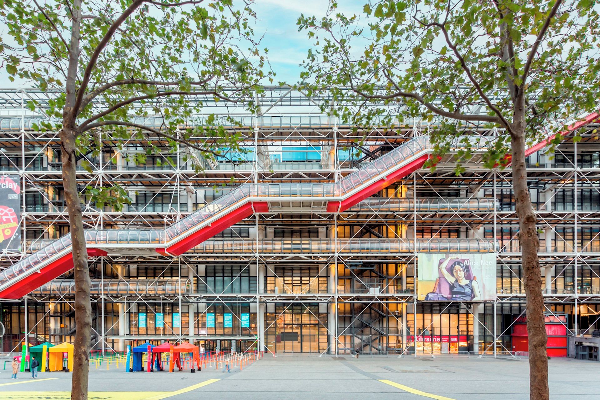 Un bâtiment moderne à plusieurs niveaux, doté d’une façade en verre et d’un escalier rouge.