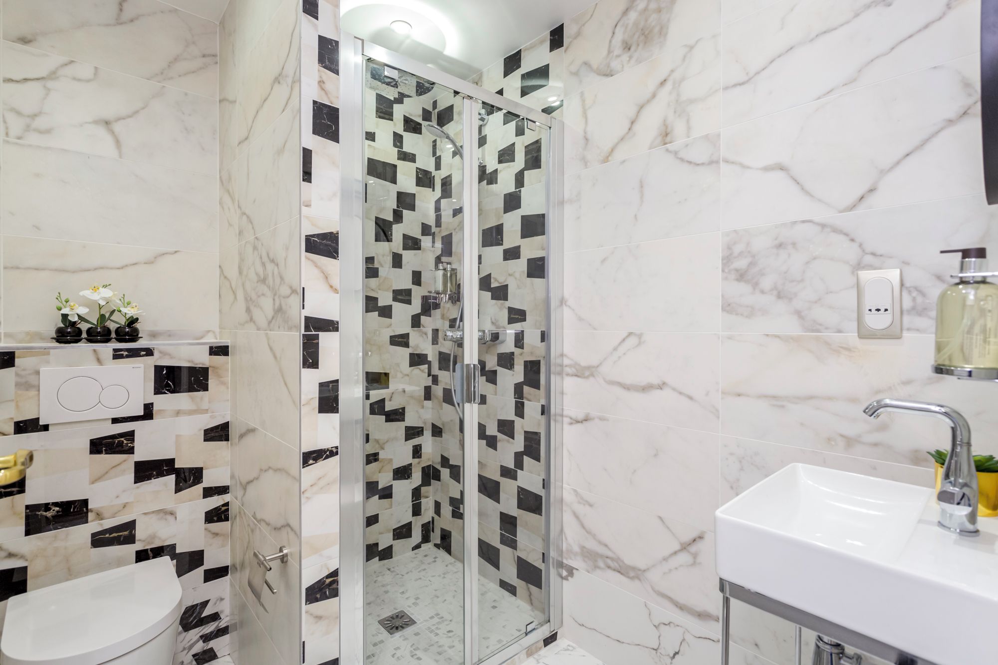Een moderne badkamer met een douchecabine van glas, een wit wastafeltje en een toilet.