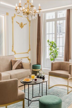 A living room with a beige sofa, two armchairs, a round coffee table, and a chandelier.