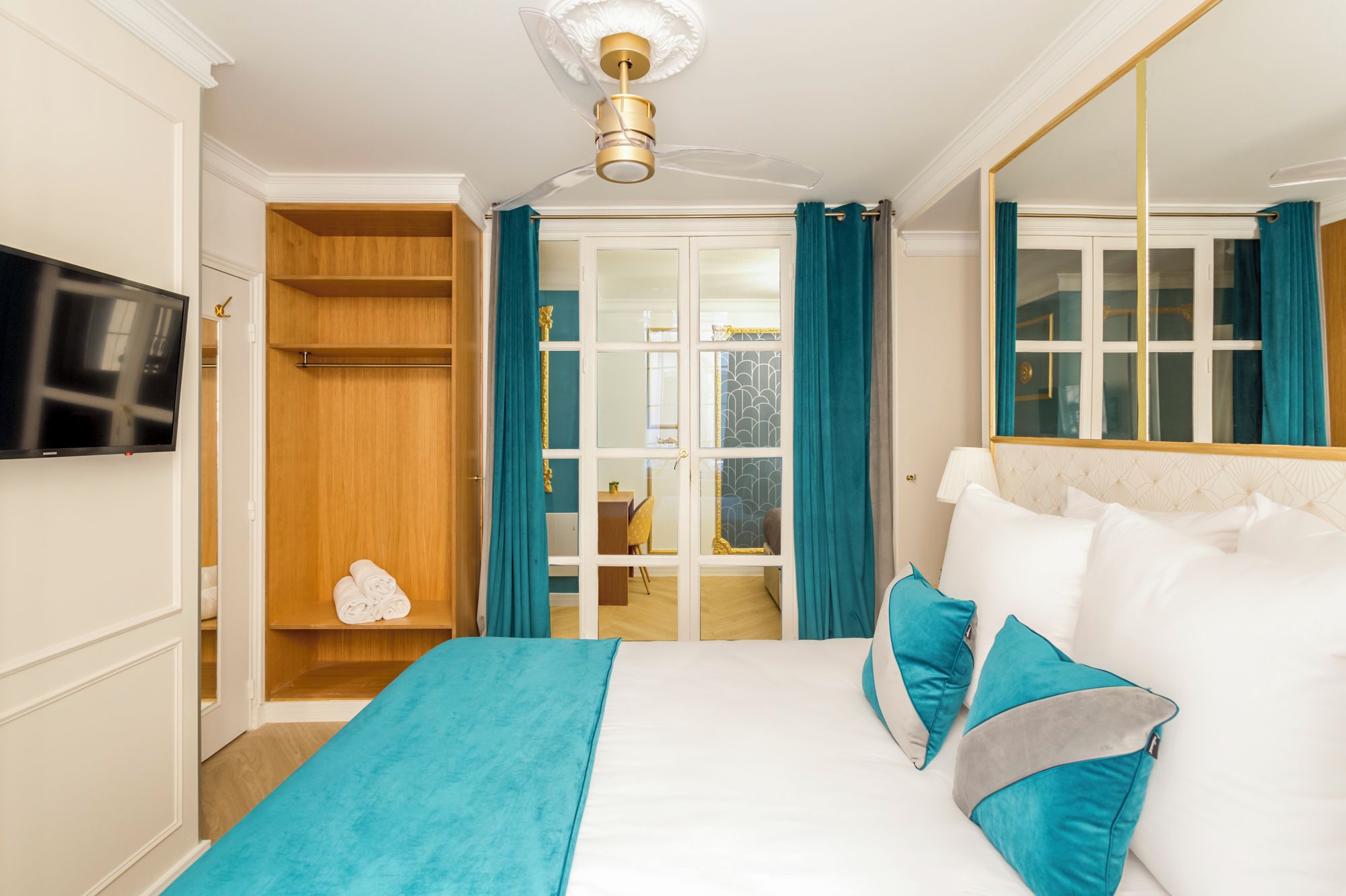 A hotel room with a bed, a TV, a wardrobe, and a bathroom visible through a glass door.