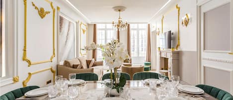 Una sala da pranzo con un tavolo in marmo apparecchiato per sei persone, dettagli dorati sulle pareti e un lampadario.