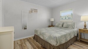 Un dormitorio con cama, mesita de noche, lámpara, espejo y ventana con persianas.