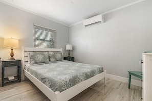 Een slaapkamer met een bed, nachtkastjes, een lamp, een raam met zonwering en een airconditioning.