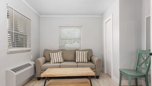 A small, well-lit room with a beige sofa, two pillows, a wooden coffee table, a green chair, and a radiator. - 2-Bedroom Condo with screened patio - Manatee - Welcome to our newly renovated, spacious and luxurious two-bedroom condo! (Matlacha)