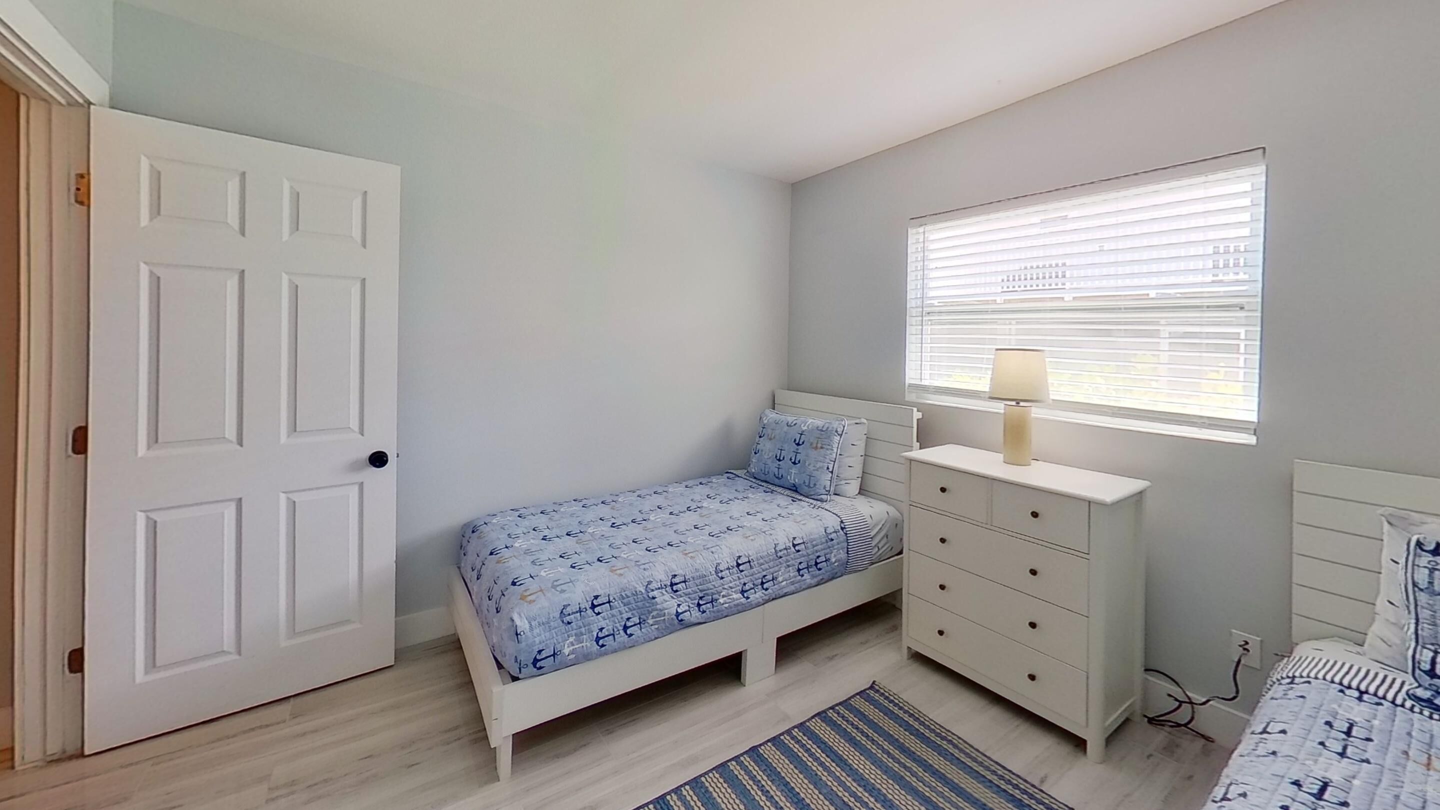 Een slaapkamer met een bed, een dressoir, een raam met jaloezieën en een deur.