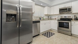 Cozinha moderna com eletrodomésticos de aço inoxidável, armários brancos e bancada de granito.