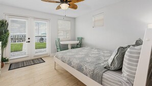 Um quarto com uma cama, ventilador de teto, mesinha e uma cadeira.