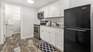 Una cocina moderna con armarios blancos, un refrigerador negro, un microondas de acero inoxidable y un horno empotrado.