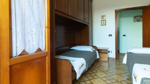 A room with two beds, wooden cabinets, a tiled floor, and a door leading to another room. - Vacation Apartment Samari Three (Gallipoli)