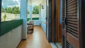 A narrow corridor with a tiled floor, a small table and chairs, a wall-mounted light fixture, and a partially open door with horizontal blinds. - Vacation Apartment Samari Three (Gallipoli)