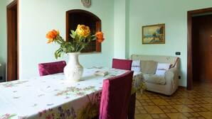 A dining area with a table set for two, a vase with flowers, and a sofa in the background. - Vacation Apartment Samari Three (Gallipoli)