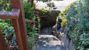 Uma escadaria de pedra estreita que desce, cercada por vegetação exuberante e uma estrutura de madeira à esquerda.