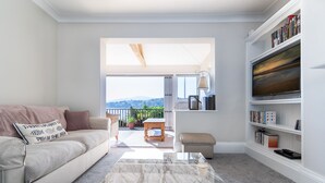 Uma sala de estar com sofá, mesa de centro, estante e vista para o exterior.