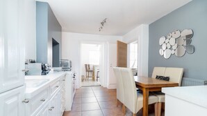 Uma cozinha moderna com armários brancos, uma área de jantar com mesa e cadeiras de madeira e uma parede azul claro com decoração em espelho.