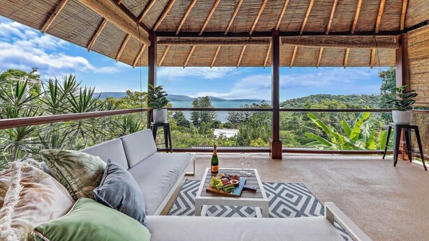 Ein Balkon mit Meerblick, eine Couch, ein Tisch mit Flasche und Gläsern sowie Kübelpflanzen.