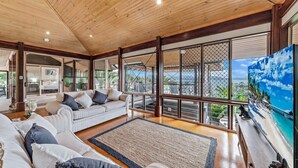 Ein geräumiges Wohnzimmer mit hoher Decke, großen Fenstern und Blick ins Freie.