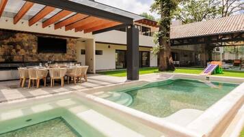 A modern outdoor pool area with a stone wall, a dining setup, and a pergola.