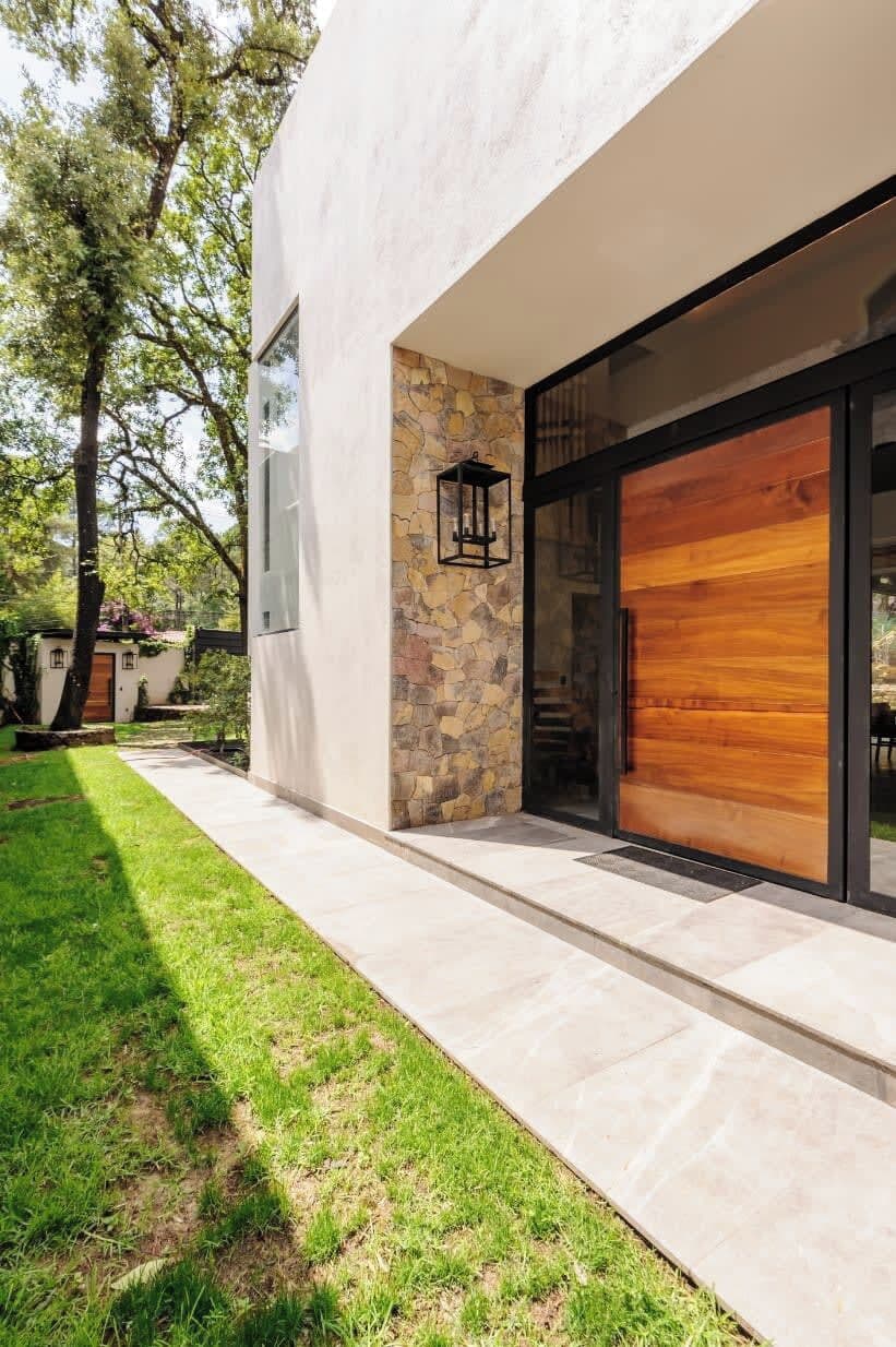 A modern house with a stone facade, a large wooden door, and a well-maintained lawn.