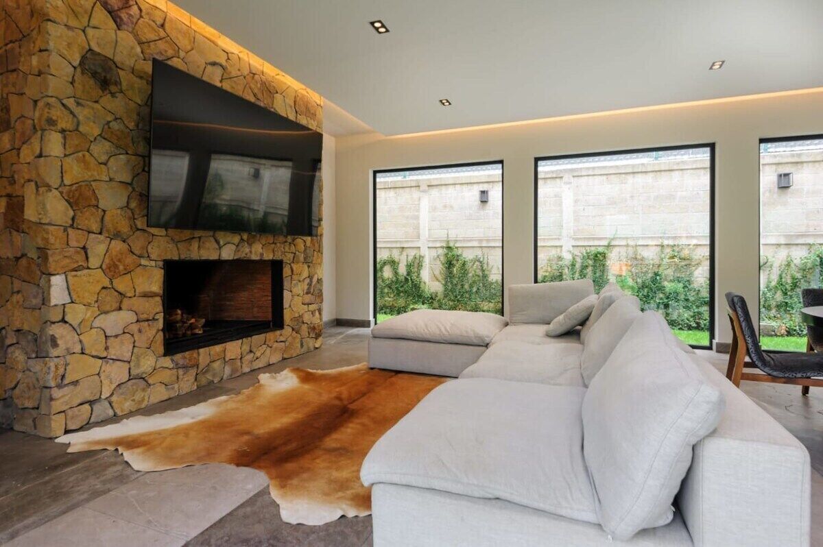 A modern living room with a stone fireplace, a large white sofa, and a leather rug.