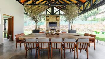 A spacious dining area with a large wooden table and chairs, a stone fireplace, and a view of the outdoors.