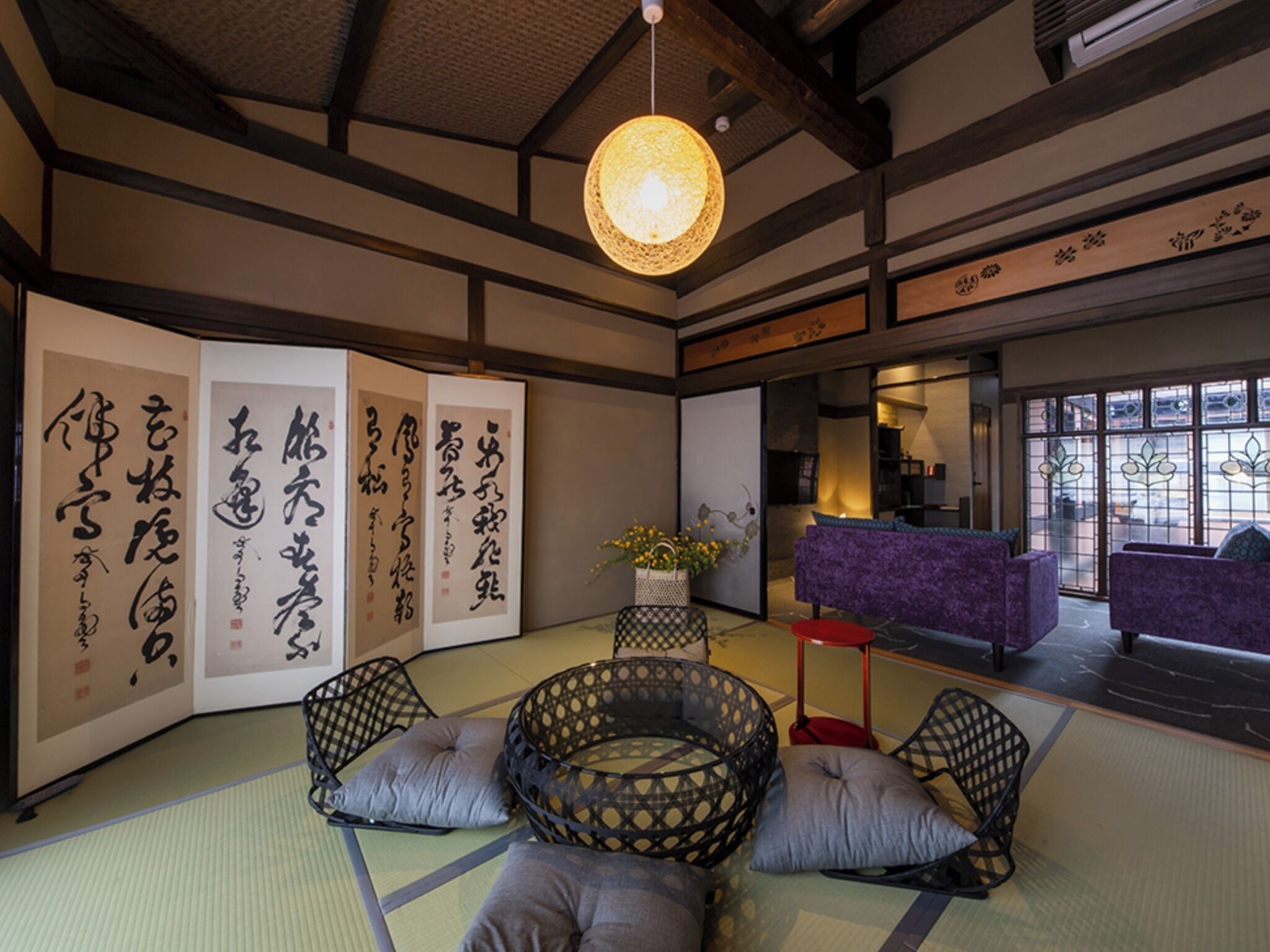 Une pièce de style japonais traditionnel, avec un sol recouvert de tatamis, une table basse avec des coussins et des calligraphies sur les murs.