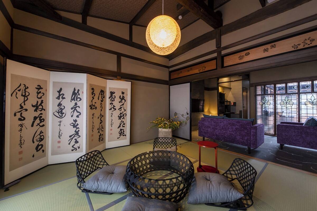 Una habitación tradicional japonesa con suelo de tatami, una mesa baja con cojines y caligrafía en las paredes.