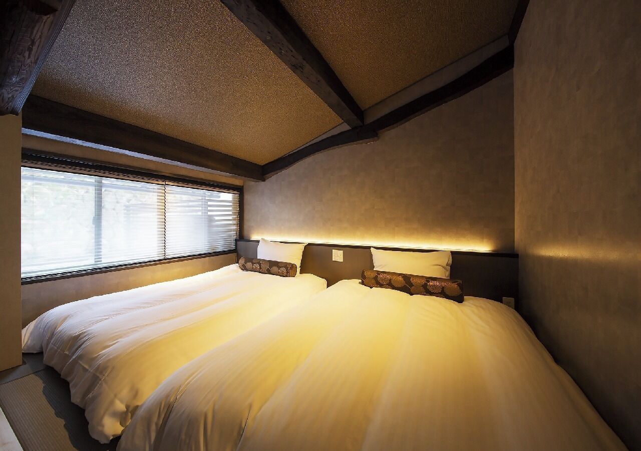 Une chambre à coucher avec un grand lit, une tête de lit dotée d’un éclairage intégré et une fenêtre avec des stores.