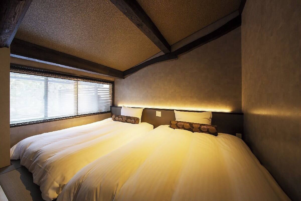 Un dormitorio con una cama grande, cabecera con iluminación integrada y ventana con persianas.