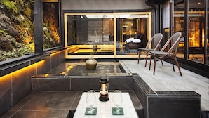 A modern outdoor seating area with a glass enclosure, a stone planter, and a table with two glasses.