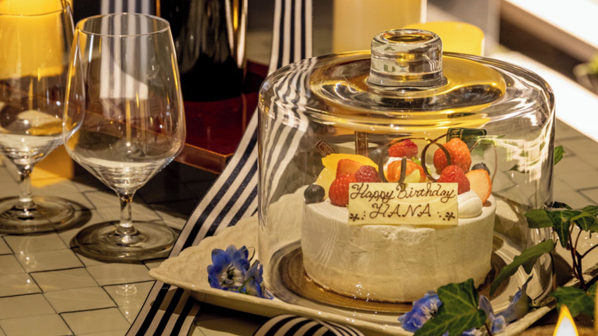 A dessert table with a birthday cake, glasses, and a candle.