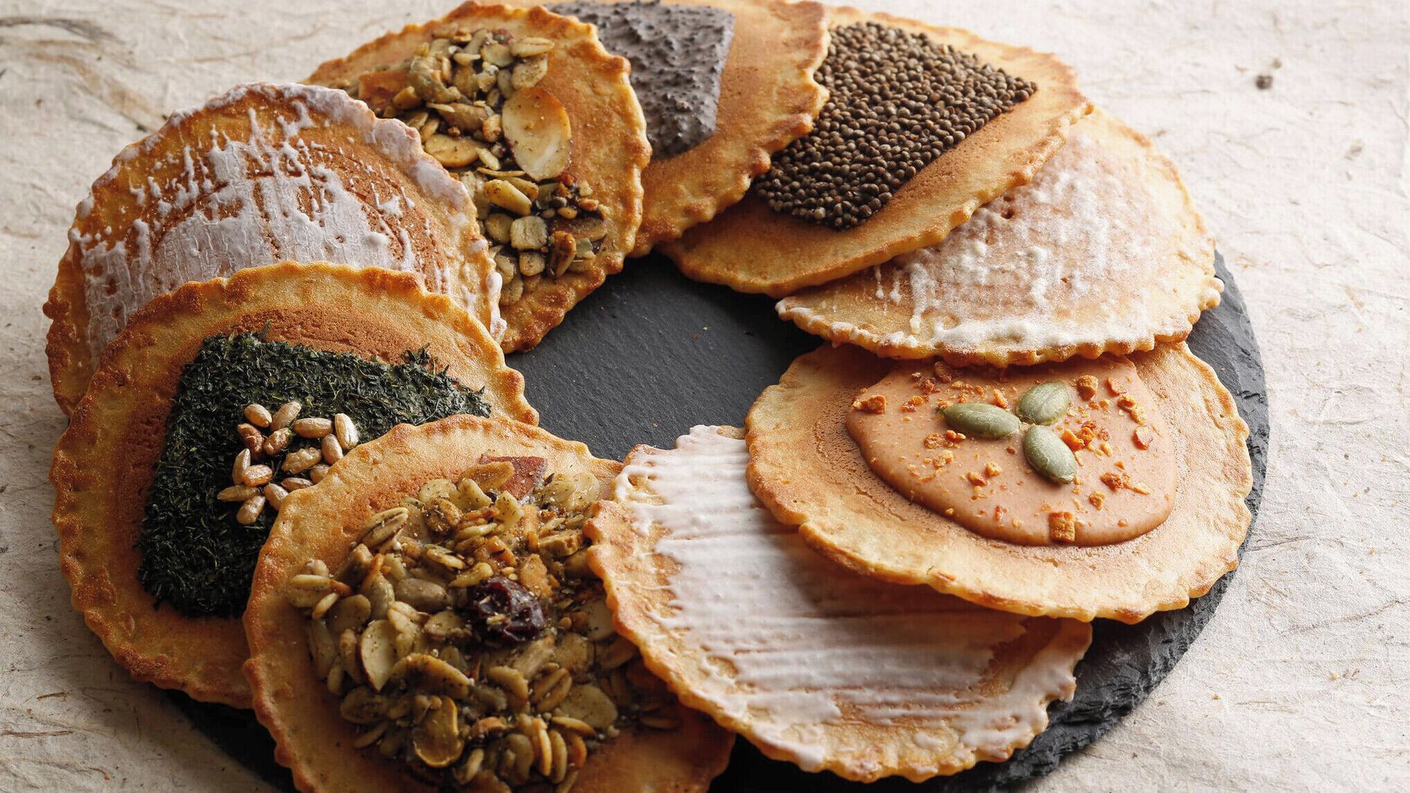 A variety of flatbreads with different toppings, arranged on a slate plate.