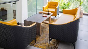 A modern living room with a glass coffee table, two black armchairs, one yellow armchair, and a large window with a view of greenery. - CASA BIANCA (Accra)