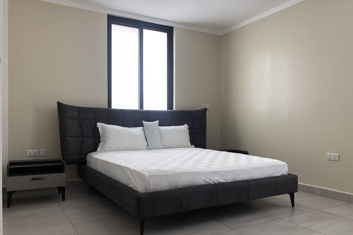 A modern bedroom with a large bed, a nightstand, and a window.
