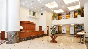Un hall espacioso con suelo de mármol, mostrador de recepción y un gran jarrón con flores.