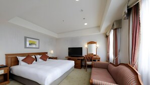 Habitación de hotel con una cama grande, un escritorio con televisor, un sofá y una ventana con cortinas.