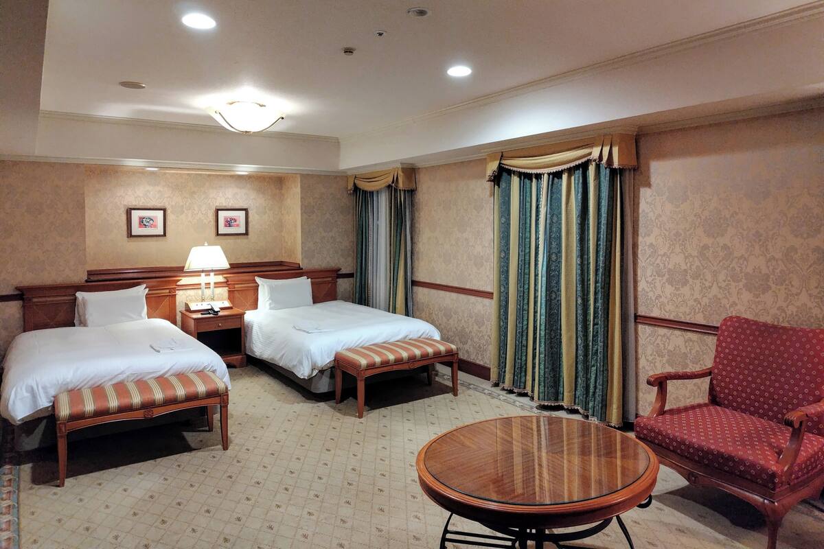 Habitación de hotel con dos camas, una silla, una mesa redonda y una lámpara.