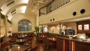 Un amplio vestíbulo de hotel con techo alto, un área de descanso central, un bar con máquina de café y una exhibición de vinos.
