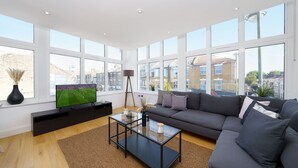 A modern living room with a large window, a flat-screen TV, a dark sofa, and a glass coffee table. - Panther House by Oval (London)